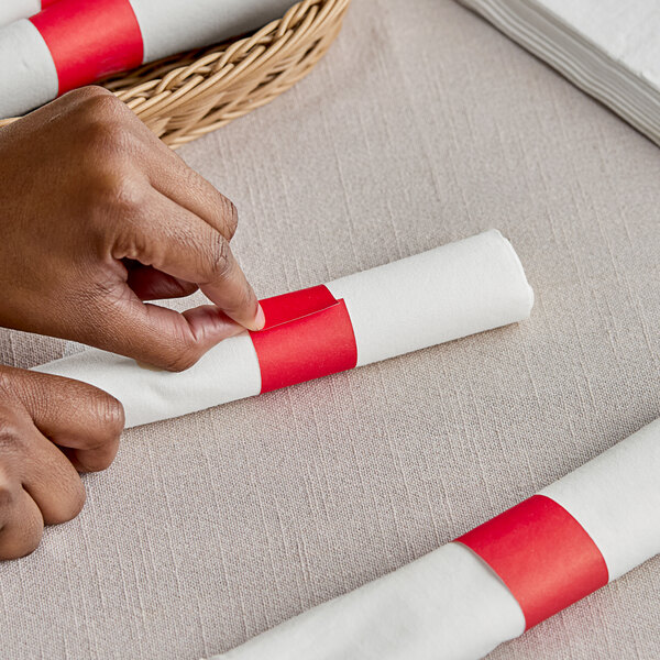 A person's hands wrapping a white napkin with a red Choice paper band.