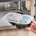 A hand holding a Choice black rectangular microwavable container with food inside.