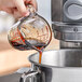 A person pouring Butternut Mountain Farm Processing Grade Pure Maple Syrup into a pot.